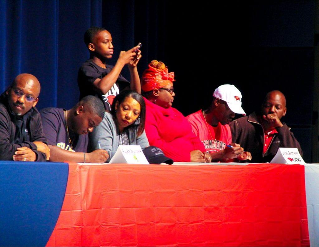 Allen Williams (Left) and Jalen Smothers (Right) sign their college contracts as their families look on. Williams is going to Texas Lutheran University and Smothers is going to the University of Incarnate Ward.